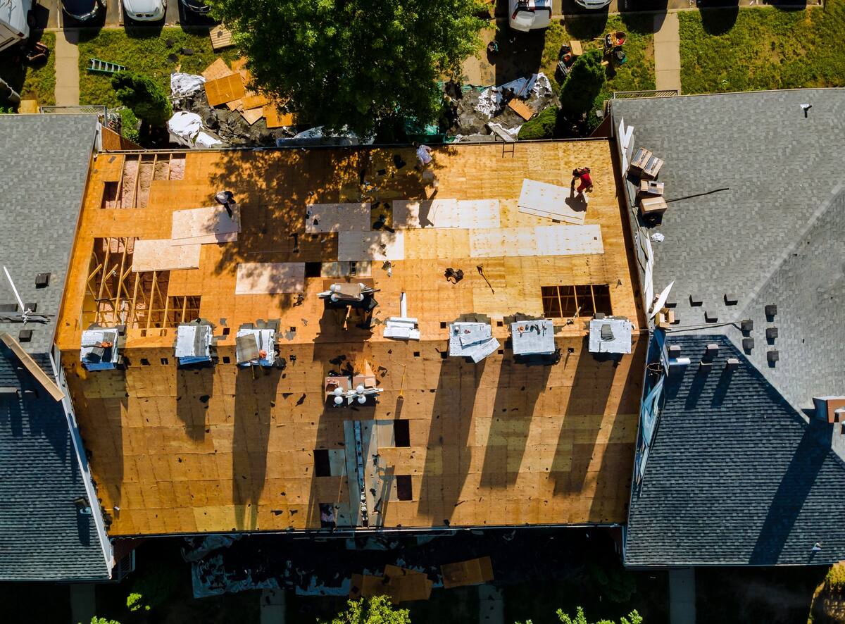 Aerial view over a home mid roof replacement, gold decking exposed with the crew at work